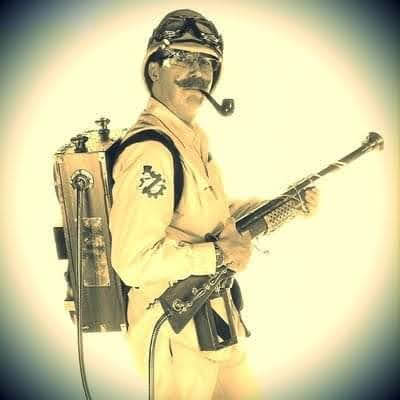 Sepia toned photograph of a man in cosplay as a steampunk ghostbuster with brass and wood proton pack and pith helmet