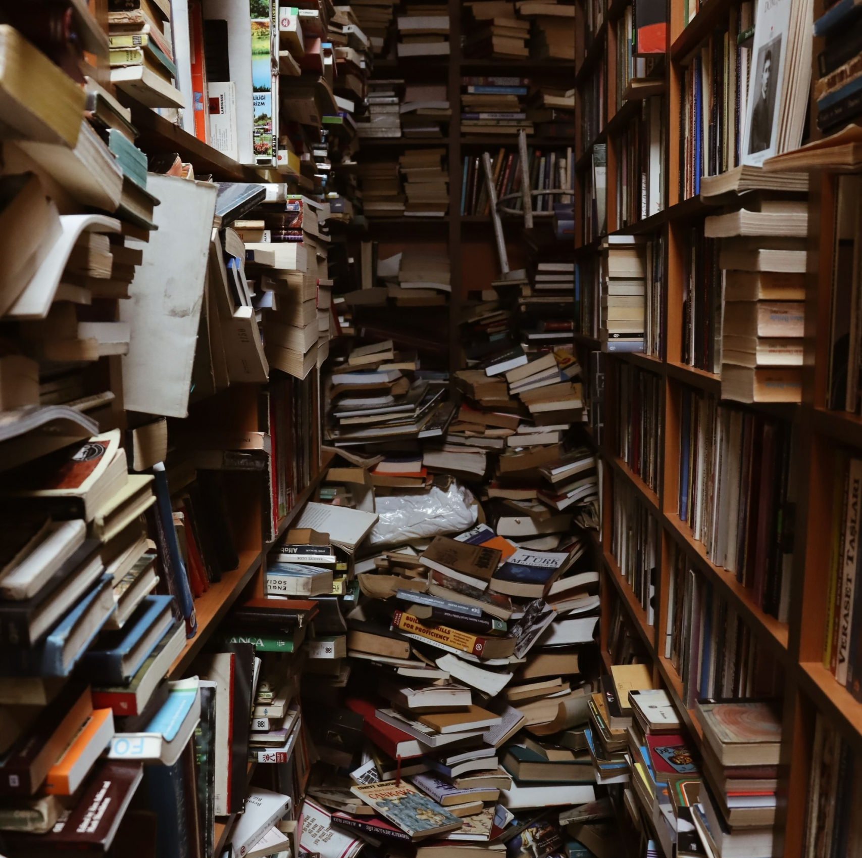 messy bookshelves with piles of books piled on floor