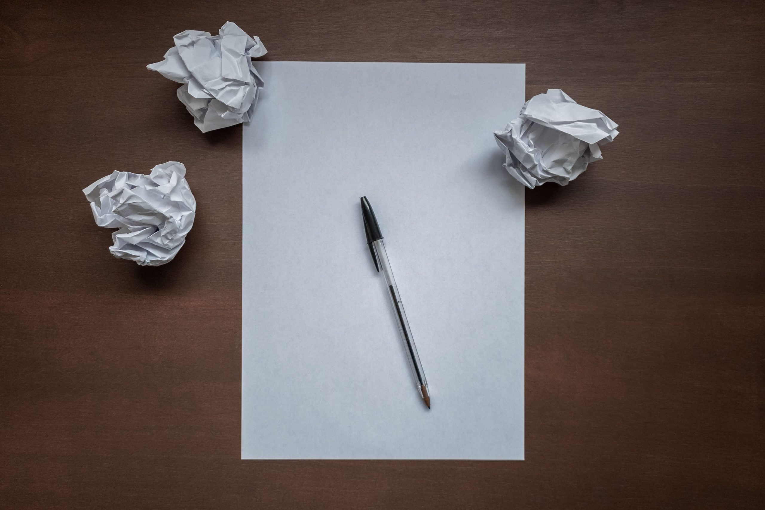 a blank page of paper and a pen. Scrumpled balls of paper sit around it.